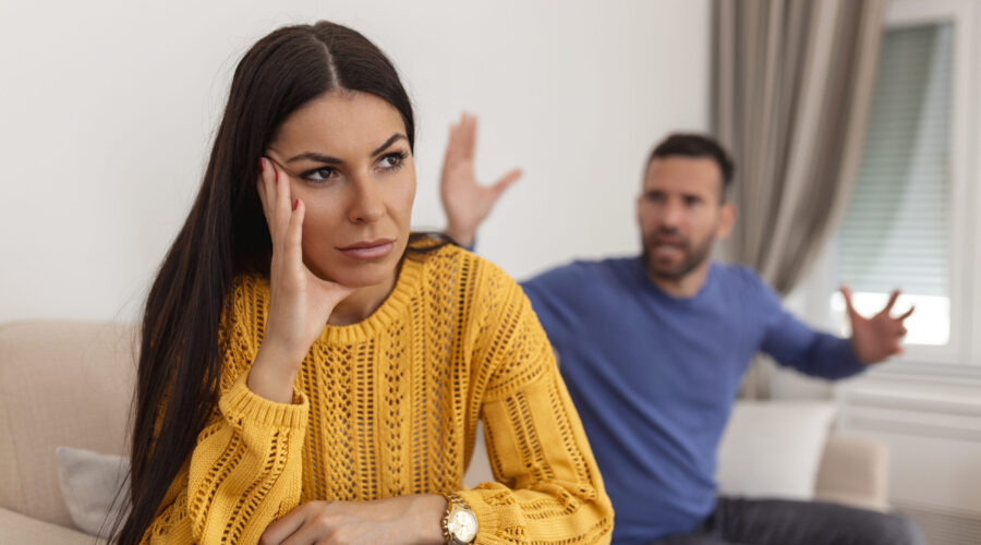 Young couple having argument - conflict, bad relationships. Angry fury woman. Angry young couple sit on couch in living room having family fight or quarrel suffer from misunderstanding